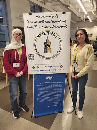 Photograph of Emily Foreman and Mariana Rojas-Montoya standing in front of a CU*iP poster.